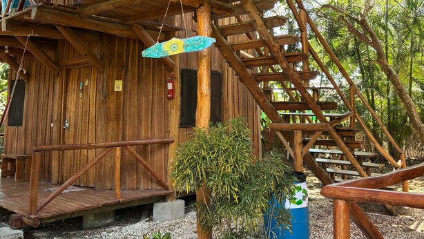 A rustic wooden structure with a wooden staircase and a hanging light fixture. - Don Jons Lodge -Surf & Yoga (Cóbano)