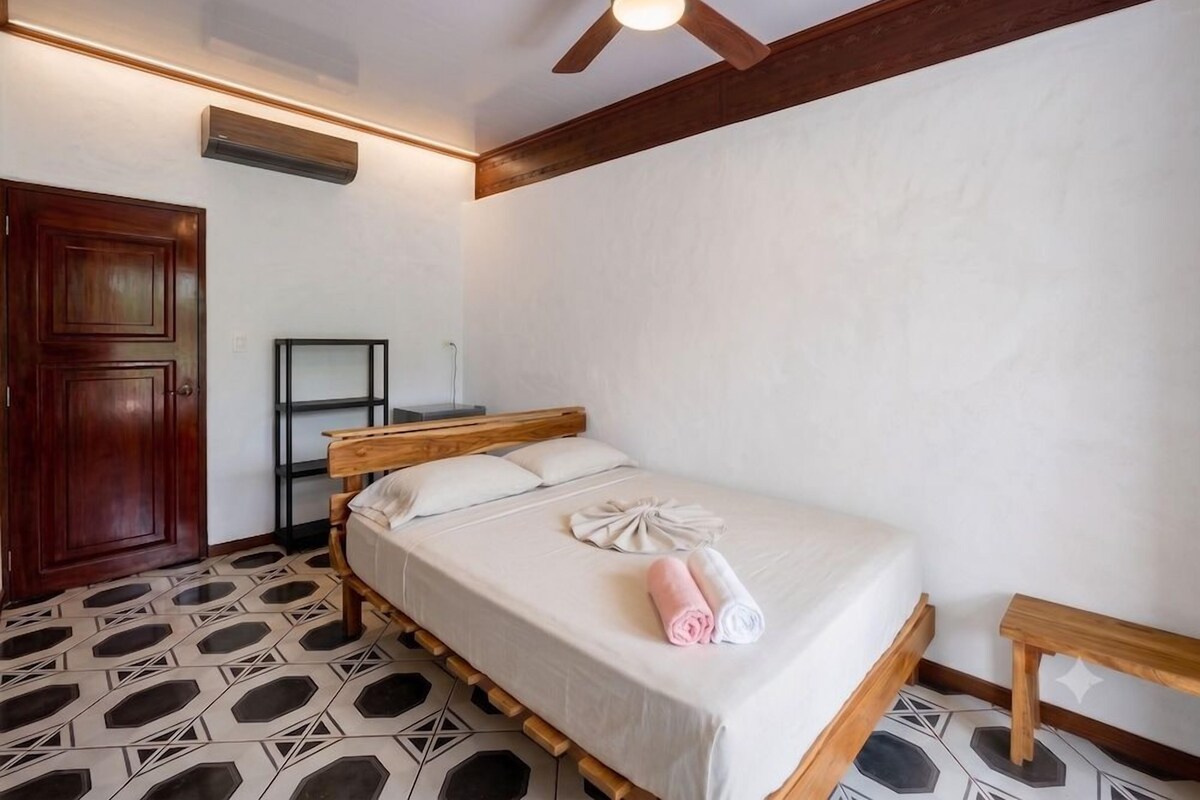 Habitación de hotel con cama, cabecera de madera, ventilador de techo, armario y piso con diseño.
