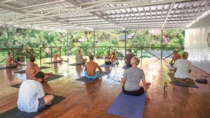 A group of people sitting on yoga mats in a spacious room with a wooden floor and a view of greenery outside. - Don Jons Lodge -Surf & Yoga (Cóbano)