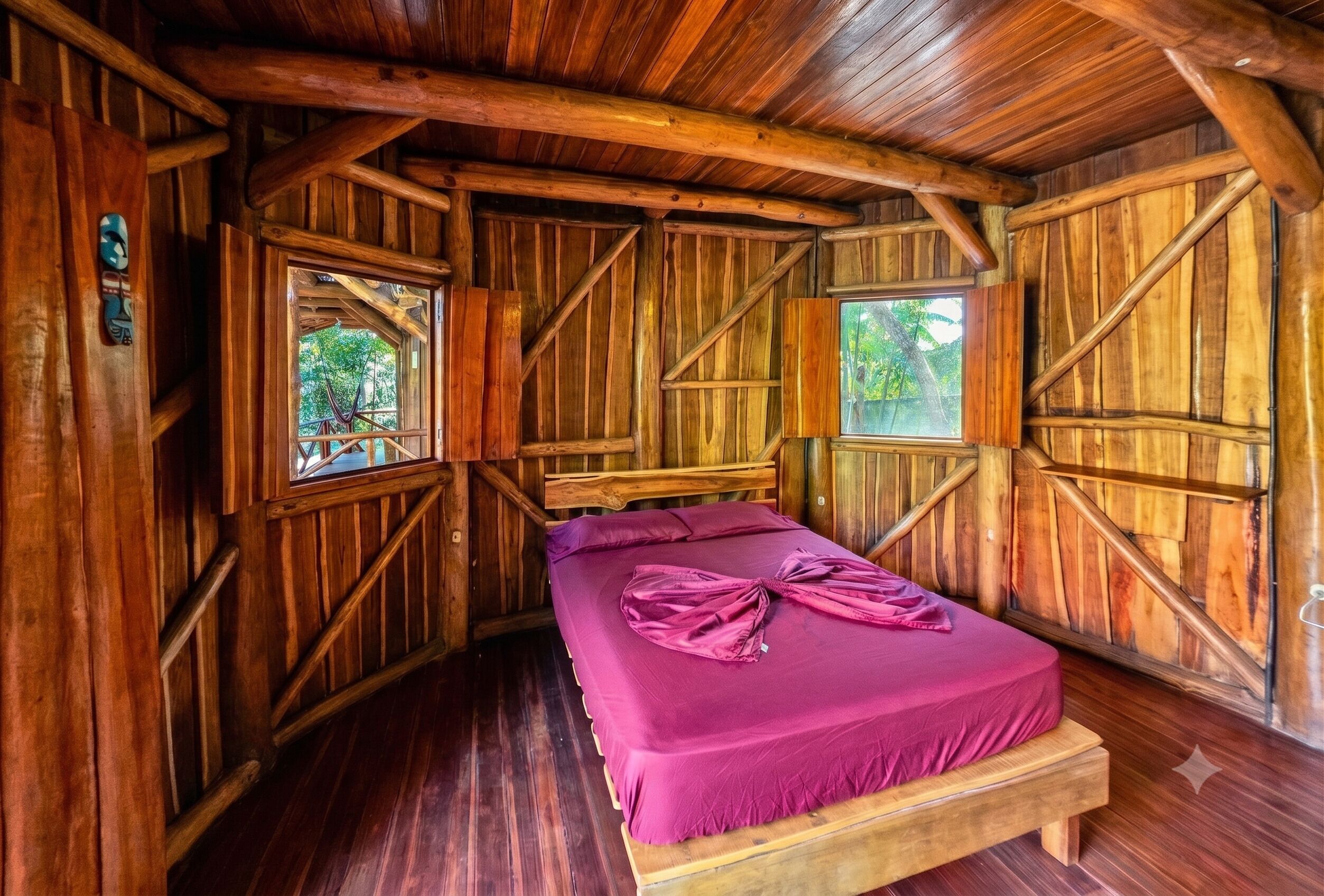 A wooden cabin room with a bed, two windows, and a hammock.