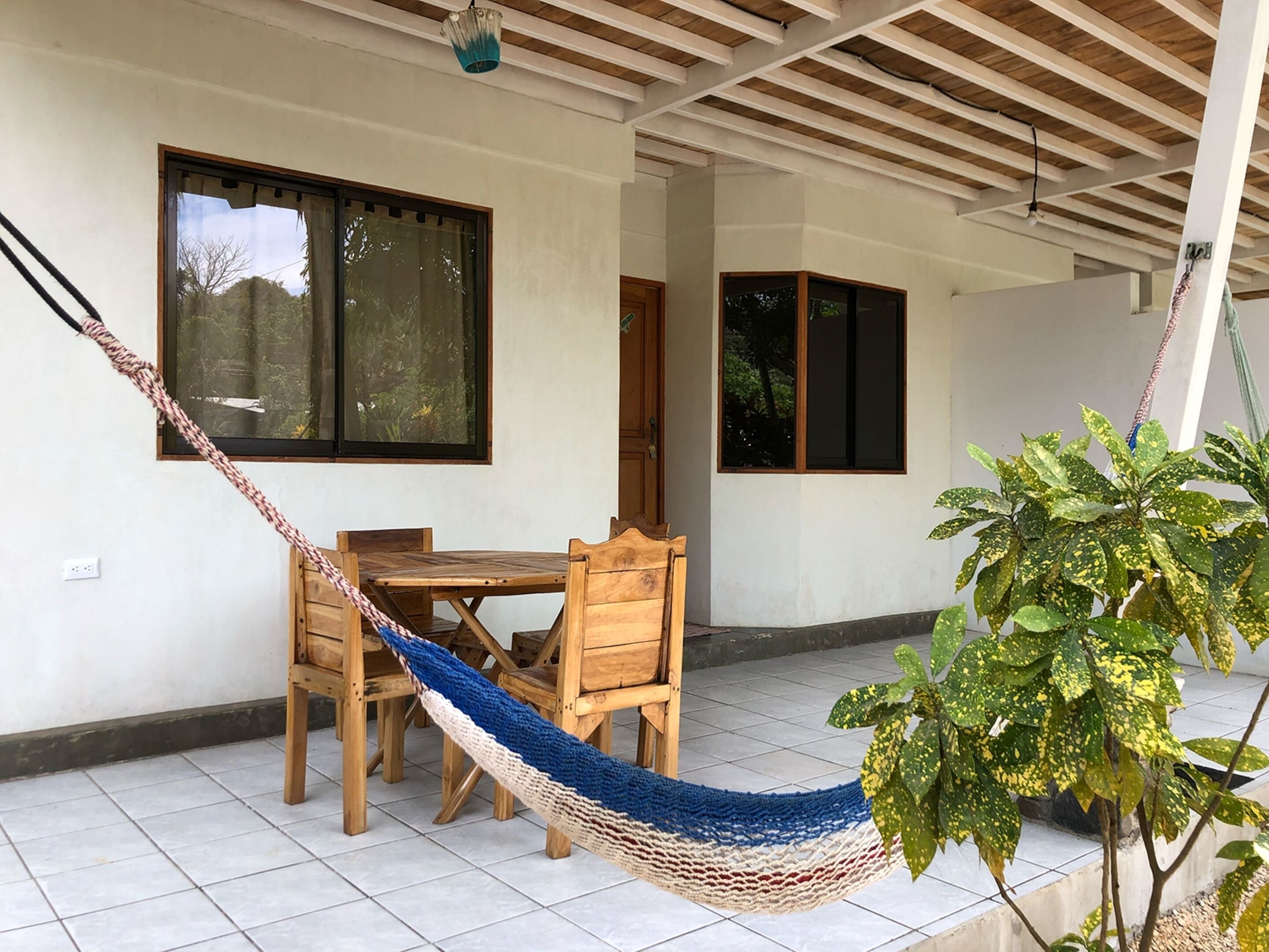 Una habitación con una mesa y sillas de madera, una hamaca y una planta en maceta.