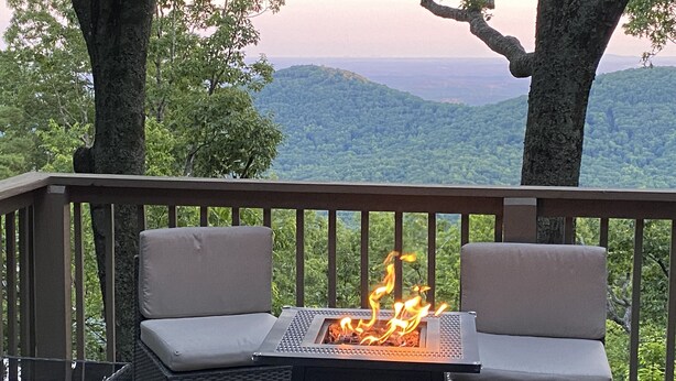 A deck with two cushioned chairs facing a fire pit, surrounded by trees and a view of distant hills. - Beautiful Views, Arcade, Shuffleboard, Pinball, 4BR 3BA - 3 King Beds (Big Canoe)