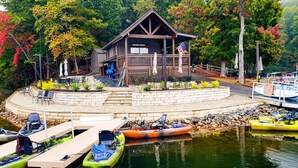 A lakeside lodge with a wooden deck, outdoor seating, and kayaks docked at the pier. - Beautiful Views, Arcade, Shuffleboard, Pinball, 4BR 3BA - 3 King Beds (Big Canoe)