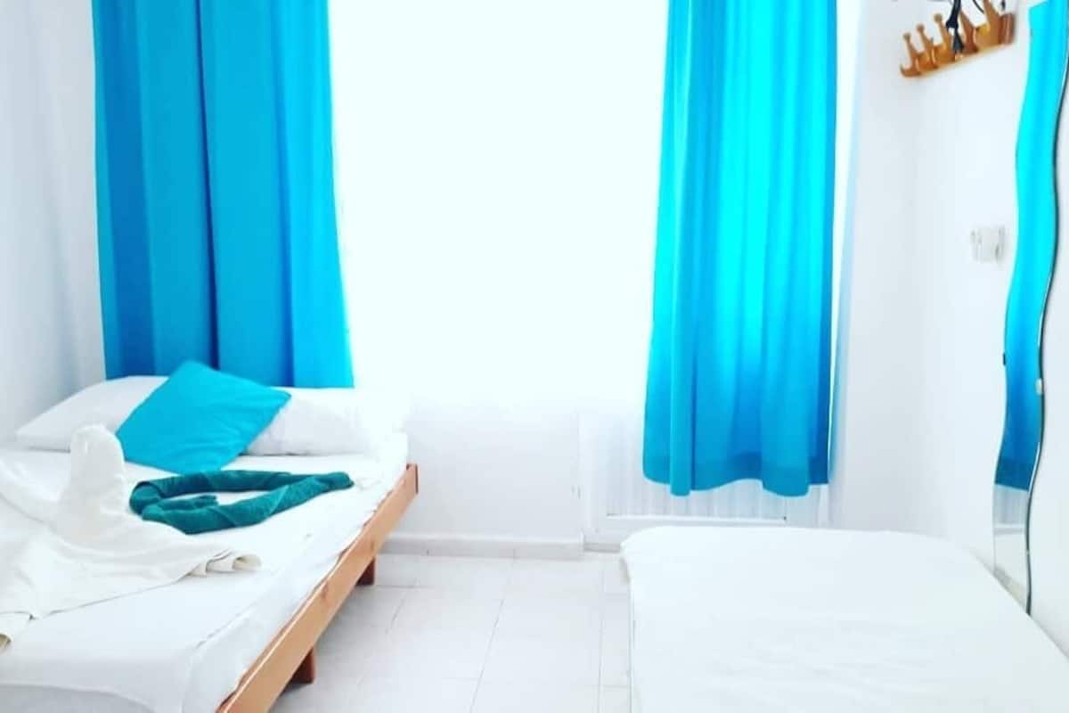 A hotel room with two beds, white bedding, and blue curtains.
