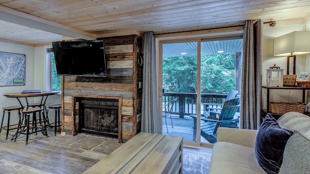 Un salon chaleureux avec une cheminée, un plafond en bois et une grande porte-fenêtre coulissante donnant sur une terrasse extérieure.