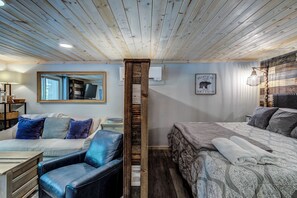 Une pièce chaleureuse avec un plafond en bois, un canapé avec des coussins bleus, un lit avec une literie à motifs et une petite table avec une lampe.