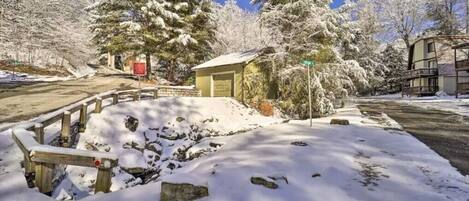 A snow-covered landscape with a wooden fence, a small building, and snow-laden trees.