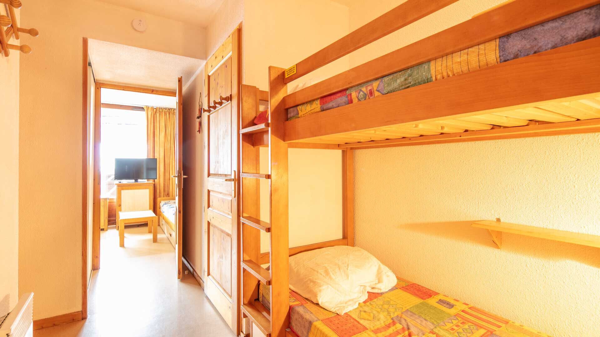 A bunk bed room with a desk and chair, a television, and a wardrobe.