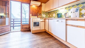 Une cuisine avec des meubles de rangement en bois, une cuisinière, un lave-vaisselle et une fenêtre donnant sur les arbres.