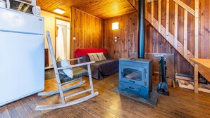 L’intérieur d’un chalet accueillant, avec un décor en bois, un canapé, un fauteuil à bascule, un poêle et un escalier.