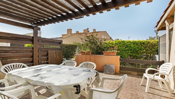 Un patio exterior con una mesa y sillas, una pérgola de madera y vistas a una casa y follaje.