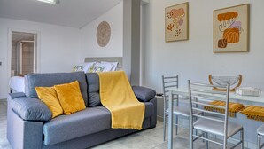Ein modernes Wohnzimmer mit einem grauen Sofa, einer gelben Decke und einem Essbereich mit Metallstühlen und einem Glastisch.