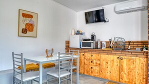 Eine kompakte Küche mit Mikrowelle, Toaster und Spüle. Ein Esstisch mit Stühlen und einem kleinen Teppich sind ebenfalls vorhanden.