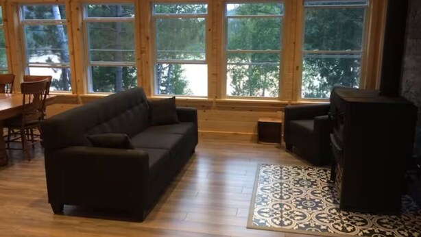 Ein großzügiges Wohnzimmer mit einem großen Fenster, einem dunklen Sofa, einem gemusterten Teppich und einem Kamin.