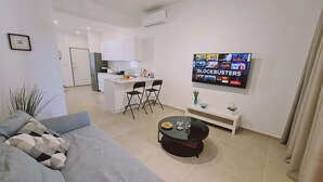 A modern living room with a grey sofa, a coffee table, and a TV displaying 'BLOCKBUSTERS'. - STAY Anemone 20 (Protaras)
