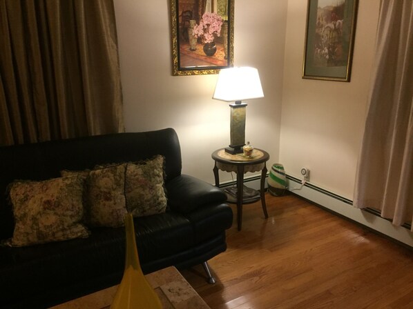 A living room with a black sofa, a lamp on a small table, and a vase with flowers. - Duplex with private Entrance , A block from UBS Arena & Belmont Park, (Elmont)