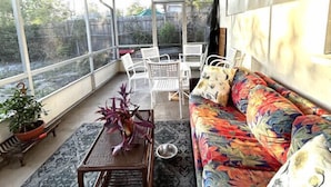 A covered patio area with a patterned rug, a wooden table with a vase, a colorful sofa, and white chairs. - Beach Break House by the Surf (Daytona Beach)