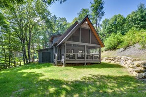 Escape to a serene cabin surrounded by a lush forest, featuring a gable roof and large windows.