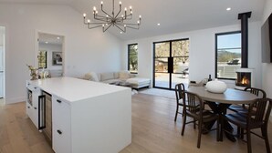 Una cocina amplia con una isla central, un área de comedor con una mesa redonda y sillas, una chimenea empotrada y ventanas grandes que ofrecen vistas al exterior.