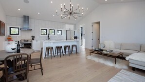 Una cocina moderna con armarios blancos, una isla central con taburetes, una zona de comedor con sillas, un sofá y una mesa de centro.