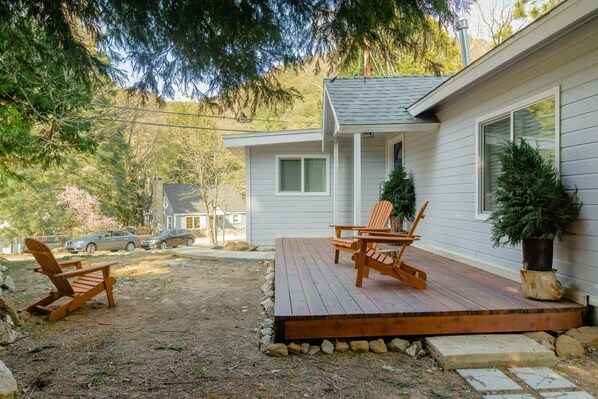 A wooden deck with two Adirondack chairs, a potted plant, and a house with a white exterior and a grey roof. - Modern Crestline Cabin Near Creek & Lake Gregory (Crestline)
