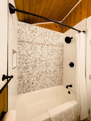Une salle de bain avec une baignoire blanche, une douche avec un mur en mosaïque et des poutres en bois au plafond.