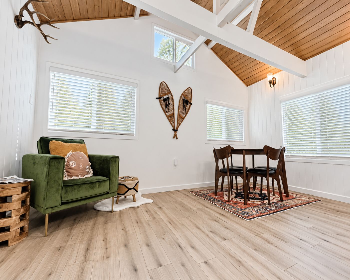 A room with a green sofa, wooden dining table, and chairs, white walls, and wooden beams on the ceiling.