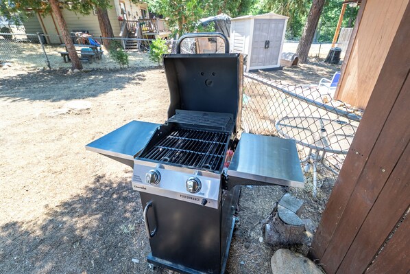 Un barbecue d’extérieur doté de deux brûleurs et d’une étagère latérale, entouré d'une clôture en treillis métallique et d'une structure en bois.