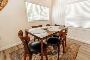 Un coin repas avec une table et des chaises en bois, un tapis et une fenêtre avec des stores.