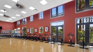Una palestra con cyclette disposte lungo il muro, ampie finestre e pavimento in legno.