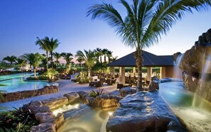 Ein Poolbereich in einem Resort mit Wasserfall, Palmen und Sitzgelegenheiten im Freien.