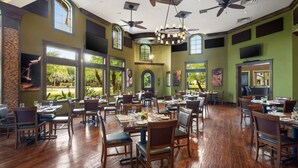 Un'ampia sala da pranzo con diversi tavoli e sedie, grandi finestre che offrono vista all'esterno e ventilatori a soffitto.