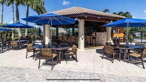 Un'area patio esterna con tavoli e sedie, ombrelloni blu e un edificio con tetto in tegole.