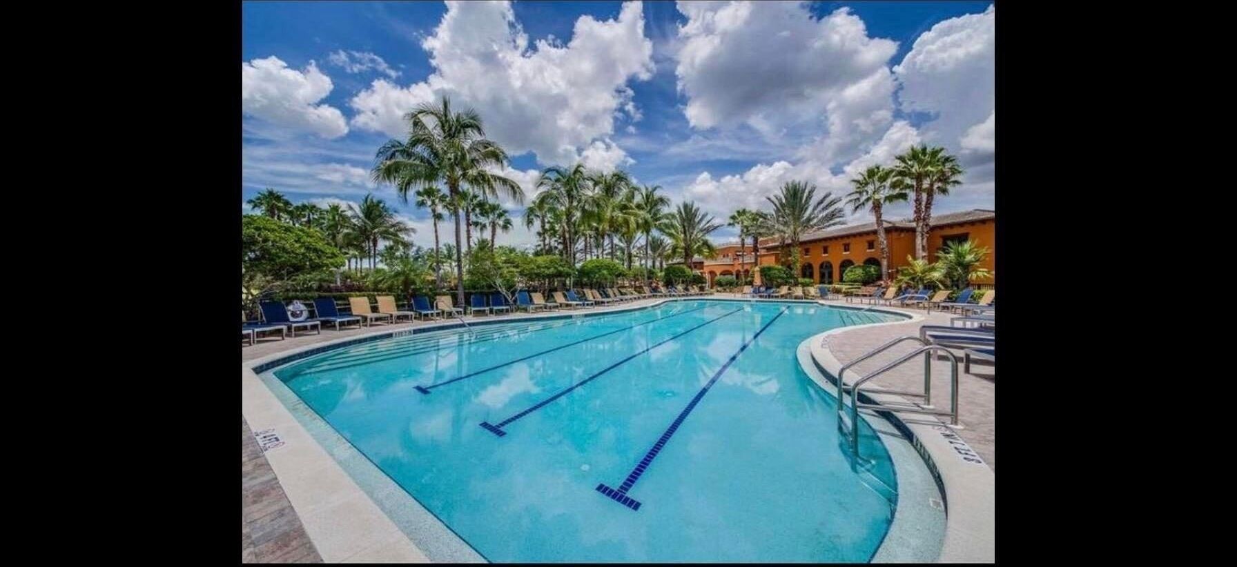 A swimming pool with clear blue water, surrounded by palm trees and lounge chairs.