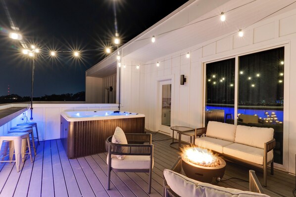Relax on the deck with a hot tub, sofa, and dining area, offering a view of the night sky and cityscape.