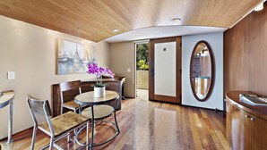 A modern interior with a wooden ceiling, a round dining table with chairs, a potted plant, and a large mirror.