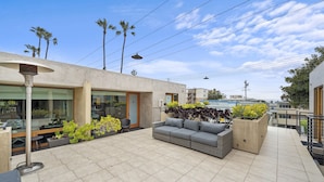 A modern outdoor patio area with a sofa, potted plants, and a view of a swimming pool.