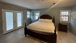 Un dormitorio con una cama grande, dos ventanas, un ventilador de techo y una mesita de noche.
