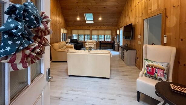 Un salón comedor amplio con techo de madera, una zona de estar central con sofá y sillones, una mesa de comedor y un televisor montado en la pared.