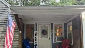 Una casa con un porche, dos sillas, una bandera estadounidense y un cartel que dice 'WELCOME'.