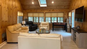 Un salón amplio con paredes y techo de madera, un sofá, una mesa de centro, una chimenea y un televisor.