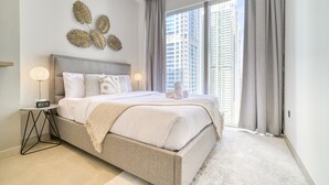 A modern bedroom with a large bed, a nightstand, a wall-mounted clock, and a city view through large windows.
