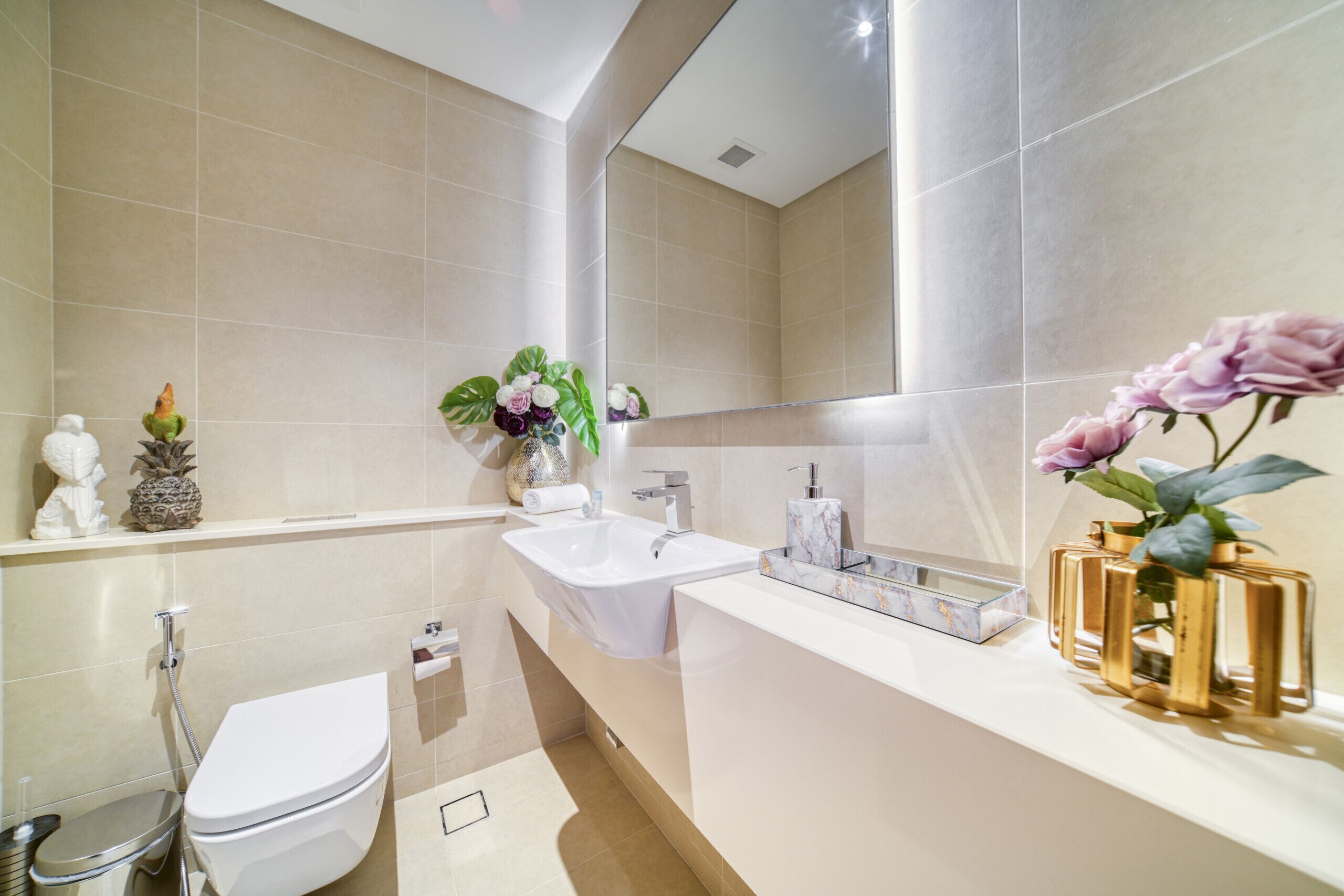 Une salle de bain moderne avec un lavabo, des toilettes et une douche, le tout de couleur blanche. Des plantes et des fleurs décoratives sont disposées sur le meuble-lavabo.