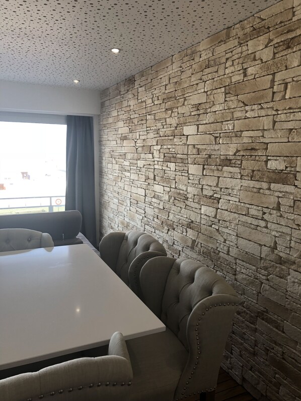 A conference room with a white table and six upholstered chairs. The room features a stone wall and a ceiling with a perforated pattern.