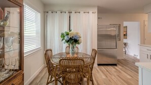Un comedor con una mesa redonda, sillas de mimbre, una mesa con cubierta de vidrio y un jarrón con flores.