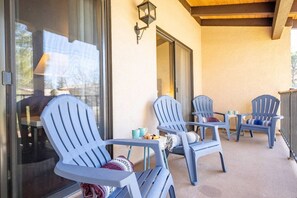Un área de estar al aire libre techada con cuatro sillas Adirondack, cada una con un cojín, y una mesita con dos tazas.