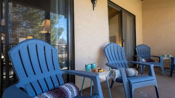 Een terras met blauwe Adirondack-stoelen, een tafeltje en een raam met uitzicht op bomen.
