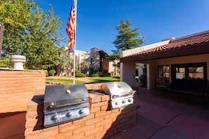 A barbecue grill setup with a flag, brick wall, and a building with a tiled roof in the background.