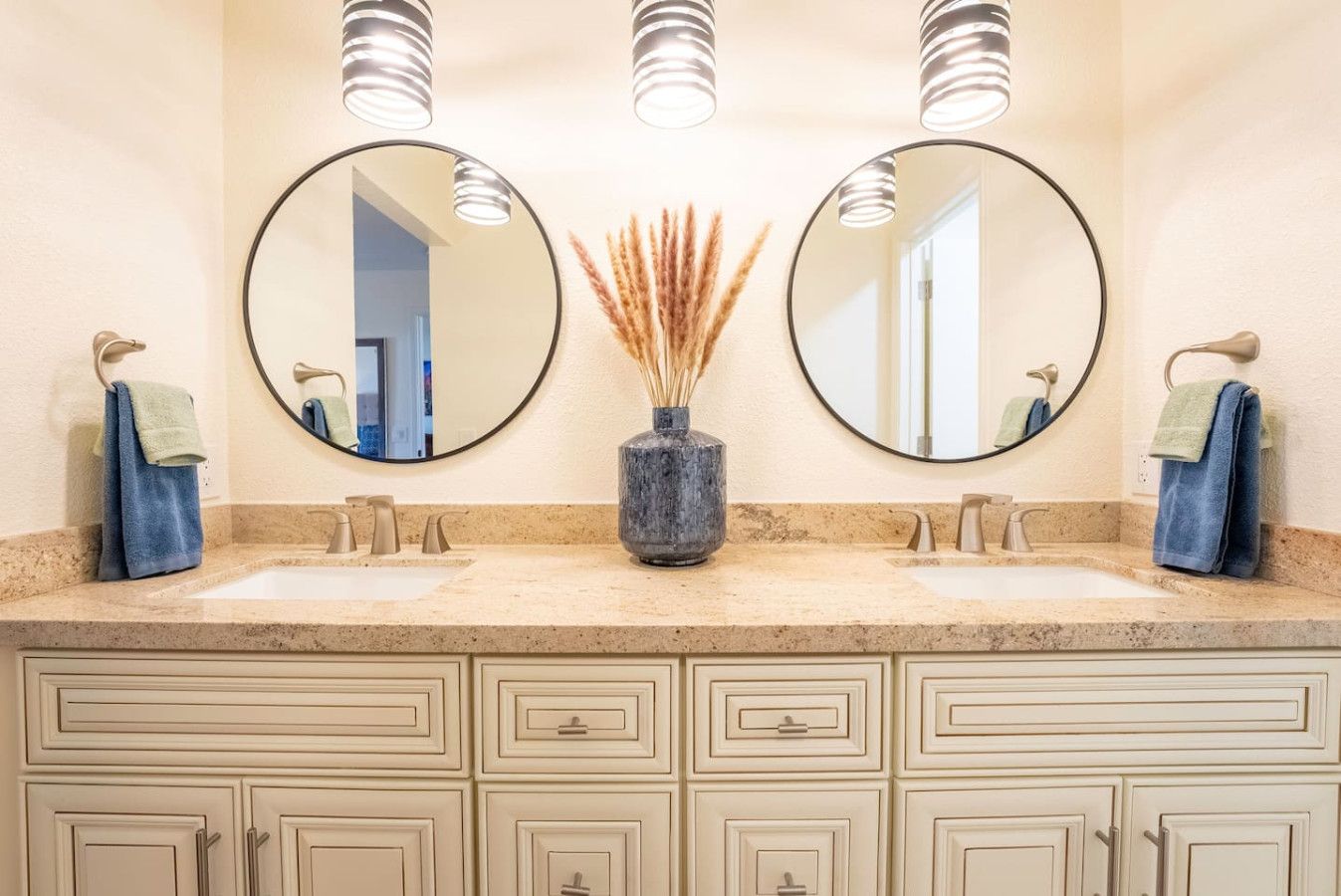 Un bagno con due specchi circolari, un vaso con piante essiccate e un piano di lavoro color beige.