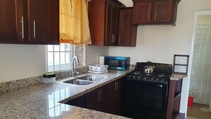 A kitchen with granite countertops, a stainless steel sink, a black stove, and wooden cabinets. - Cozy retreat pool access super close to the Town. Entire home available to you! (Old Harbour)